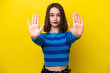 Sarı arka planda izole edilmiş genç Ukraynalı kadın dur hareketi yapıyor ve hayal kırıklığına uğruyor