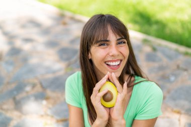Açık havada elinde avakado tutan genç bir kadın şaşırmış bir ifadeyle.