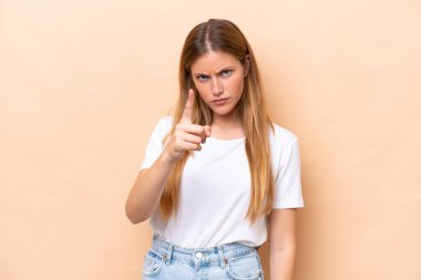 Bej arka planda izole edilmiş genç beyaz kadın hayal kırıklığına uğramış ve ön tarafı işaret ediyor.