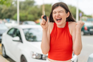 Açık havada elinde araba anahtarlarıyla genç ve güzel bir kadın zaferi kutluyor.