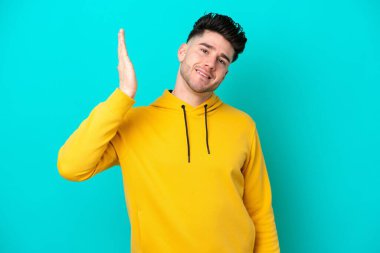 Kafkasyalı genç adam mavi arka planda izole edilmiş, yorgun ve hasta bir ifadeyle.