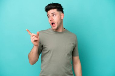 Kafkasyalı genç adam mavi arka planda izole edilmiş bir şekilde parmağını kaldırarak çözümü anlamaya çalışıyor.