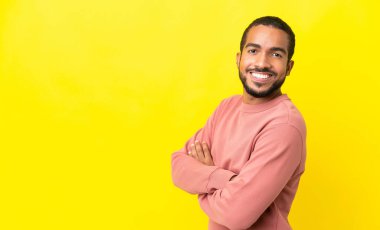 Sarı arka planda izole edilmiş, kolları çapraz ve ileriye bakan genç Latin bir adam.