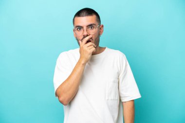 Mavi arka planda izole edilmiş genç beyaz adam sağa bakarken şaşırdı ve şok oldu.