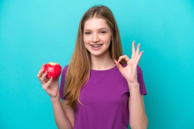 Gülümseyen kız kırmızı elma tutuyor, tamam jest yapıyor.