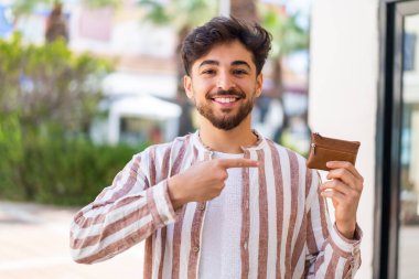 Yakışıklı bir Arap, dışarıda bir cüzdan tutuyor ve ona doğrultuyor.