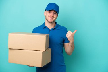 Teslimat için beyaz bir adam mavi arka planda izole edilmiş ve bir ürün sunmak için kenarı işaret ediyor.