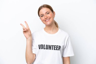 Beyaz arka planda izole edilmiş genç gönüllü kadın gülümsüyor ve zafer işareti gösteriyor.