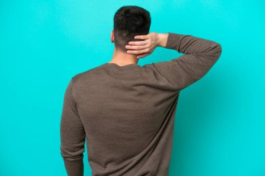 Kafkasyalı genç adam mavi arka planda izole edilmiş ve düşünüyor.