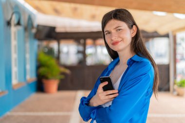 Dışarıda cep telefonu tutan ve kolları bağlı genç ve güzel bir kadın.