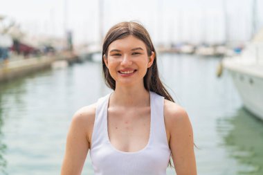 Genç, güzel bir kadın açık havada, mutlu bir ifadeyle.