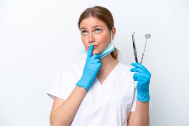Beyaz arka planda izole edilmiş aletleri tutan beyaz dişçi kadın yukarı bakarken şüphe duyuyor