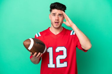 Rugby oynayan Kafkasyalı genç adam, yeşil arka planda izole edilmiş, sürpriz bir ifadeyle.