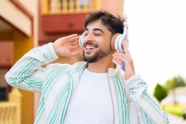 Yakışıklı bir Arap açık havada müzik dinliyor ve şarkı söylüyor.