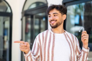Görünmez diş telleri tutan yakışıklı Arap bir ürünü sunmak için yan tarafı işaret ediyor.