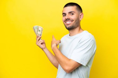 Kafkasyalı genç bir adam, sarı arka planda izole edilmiş bir sürü para alıyor.