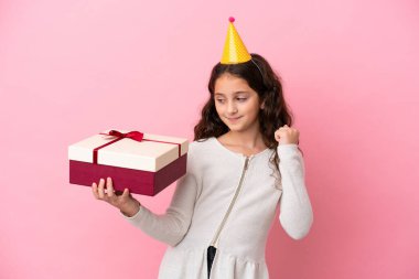 Küçük beyaz kız pembe arka planda izole edilmiş bir hediyeyle zaferi kutluyor.