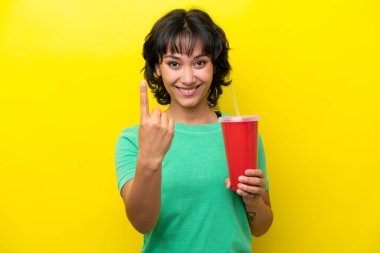 Arjantinli genç bir kadın sarı arka planda izole edilmiş bir gazoz tutuyor.