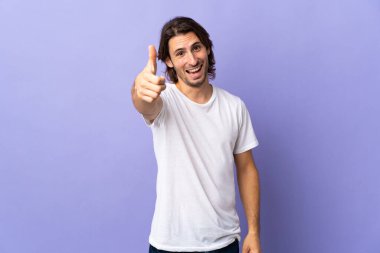 Mor arka planda izole edilmiş genç ve yakışıklı bir adam. Başparmakları havada. Çünkü iyi bir şey oldu.