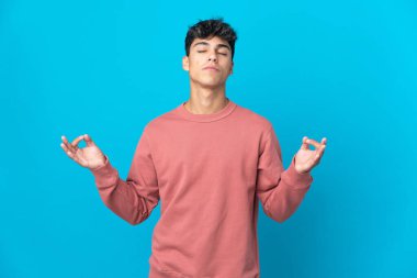 Zen pozisyonunda soyutlanmış mavi arka planı olan genç bir adam