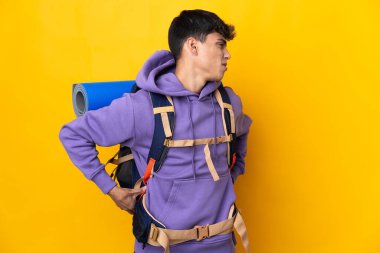 Sırt ağrısı çeken, izole edilmiş sarı arka planda büyük bir sırt çantasıyla genç dağcı çaba sarf ettiği için acı çekiyor.