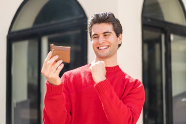 Dışarıda cüzdanı olan yakışıklı genç bir adam zaferi kutluyor.