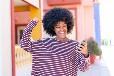 Açık havada cep telefonu kullanan Afrikalı Amerikalı bir kız zaferi kutluyor.