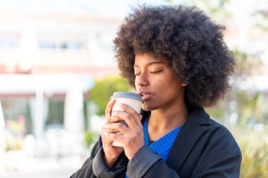 Afro-Amerikalı kız açık havada elinde kahve tutuyor.