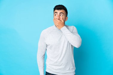 İzole edilmiş mavi arka plan üzerinde beyaz bir adam yan tarafa bakarken sürpriz jest yapıyor.