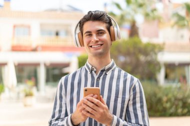 Genç yakışıklı adam müzik dinliyor cep telefonu var ve önüne bakıyor.