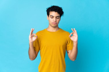 Genç Venezuelalı adam Zen pozunda mavi arka planda izole edilmiş.