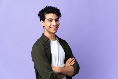 Genç Venezuelalı adam mor arka planda izole edilmiş, kolları bağlı ve ileriye bakıyor.