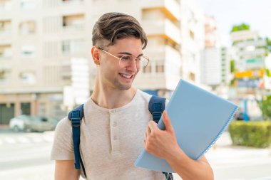 Genç ve yakışıklı bir öğrenci açık havada mutlu bir ifadeyle.