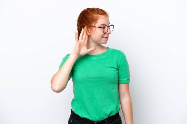 Kırmızımsı genç bir kadın beyaz arka planda izole edilmiş bir şekilde elini kulağına koyarak bir şeyler dinliyor.