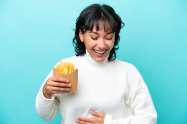 Arjantinli genç bir kadın elinde kızarmış cipslerle mavi arka planda izole edilmiş gülümsüyor.