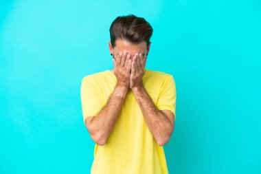 Kafkasyalı genç adam mavi arka planda izole edilmiş, yorgun ve hasta bir ifadeyle.