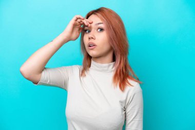 Genç Rus kadın mavi arka planda izole edilmiş. Önüne bakarken sürpriz jest yapıyor.