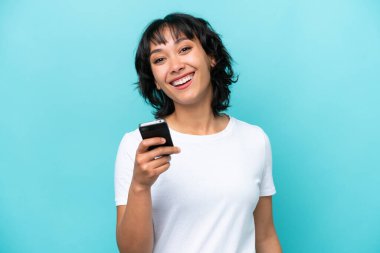 Genç Arjantinli kadın mavi arka planda cep telefonu kullanıyor.