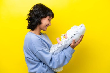 Arjantinli genç bir kadın tatlı bebeğiyle sarı arka planda izole edilmiş.