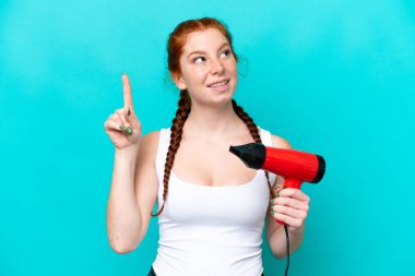 Mavi arka planda izole edilmiş bir saç kurutma makinesini tutan beyaz tenli genç, çözümün farkına varmak için parmağını kaldırıyor.