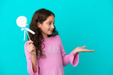 Küçük beyaz kız elinde lolipop tutuyordu. Mavi arka plandaydı ve yüzünde sürpriz bir ifade vardı.