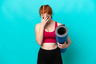 Genç spor kırmızısı kadın yoga derslerine giderken elinde mavi arka planda yorgun ve hasta bir ifadeyle bir minder tutuyordu.