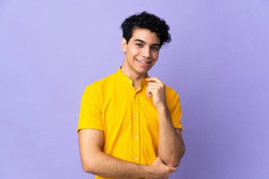 Genç Venezuelalı adam, mor arka planda izole edilmiş gülüyor.