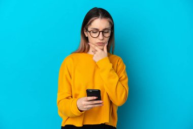 Genç beyaz kadın mavi arka planda izole edilmiş düşünüyor ve bir mesaj gönderiyor.