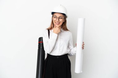 Miğferli ve elinde planları olan genç bir mimar beyaz arka planda izole edilmiş bir şekilde yan tarafa bakıyor ve gülümsüyor.