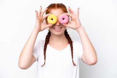 Kırmızımsı genç kadın beyaz arka planda gözlerinde donut tutarak izole edilmiş.