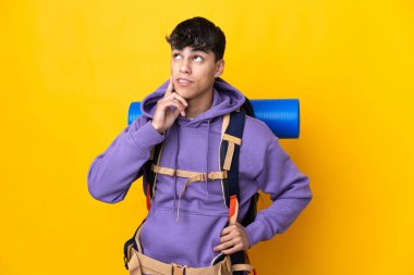 Sarı arka plan üzerinde büyük bir sırt çantası olan genç dağcı yukarı bakarken bir fikir düşünüyor.