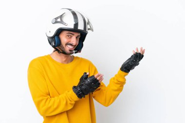 Motosiklet kasklı beyaz tenli genç adam beyaz arka planda izole edilmiş. Davet etmek için ellerini yana uzatıyor.