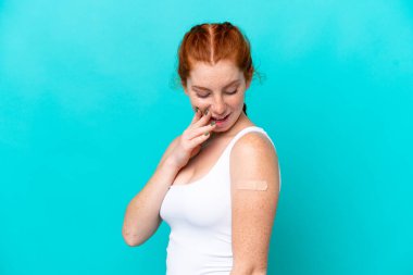 Mavi arka planda yara bandı takan genç, kırmızı bir kadın. Şaşırmış ve şok olmuş bir yüz ifadesi var.