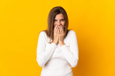 Sarı arka planda izole edilmiş genç Slovak kadın mutlu ve gülümseyerek elleri ile ağzını kapatıyor.
